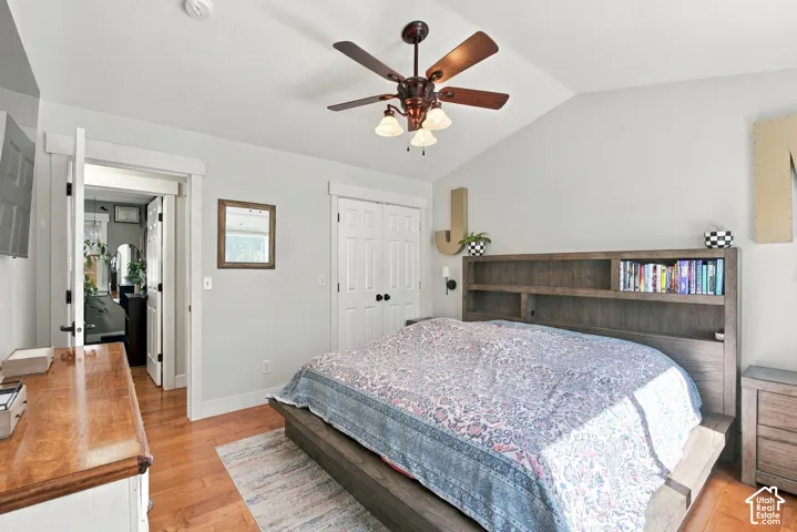 Primary bedroom wood-finish flooring, vaulted ceiling, ceiling fan with integrated lighting, and white paneled doors