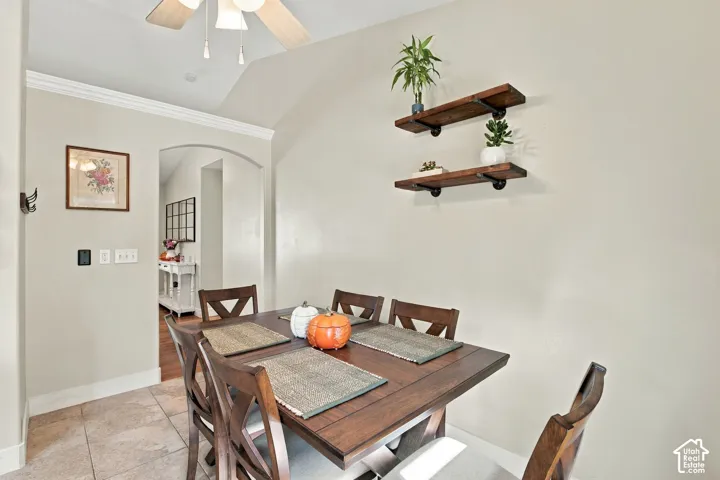 Vaulted ceiling with ceiling fan, crown molding, arched entryway, and tile flooring