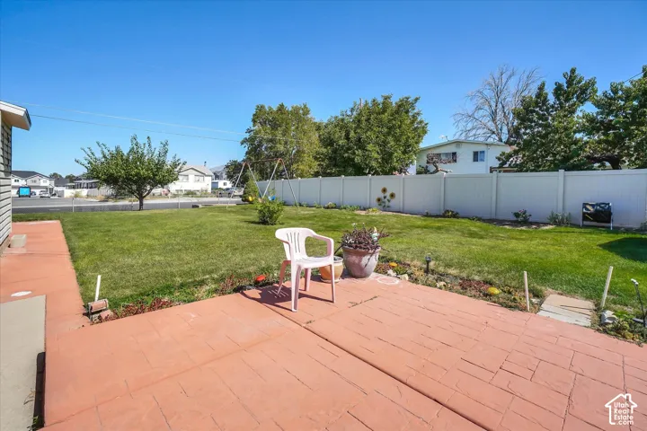 Expansive backyard featuring a large stamped concrete patio, a manicured lawn, and a white privacy fence