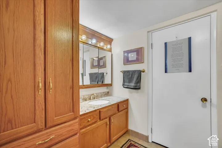 Oak cabinetry with gold-tone hardware, vanity with a rectangular sink, granite-style countertop, and a mirrored medicine cabinet with integrated lighting
