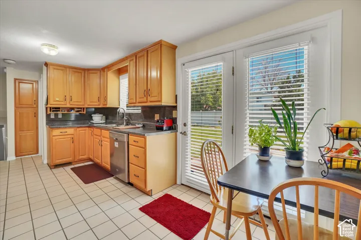 Kitchen featuring wood cabinetry, stone-finish countertops, stainless-steel dishwasher, and tile flooring