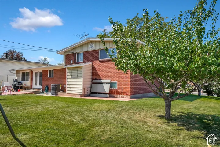 Expansive grassy yard with mature trees, brick exterior, and a paved patio area