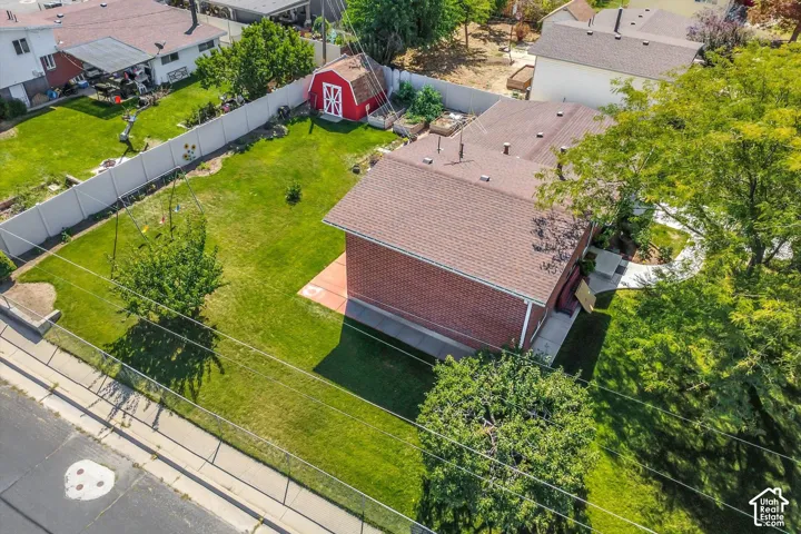 Expansive green lawn, red brick exterior, brown shingle roofing, white privacy fencing, and a red shed