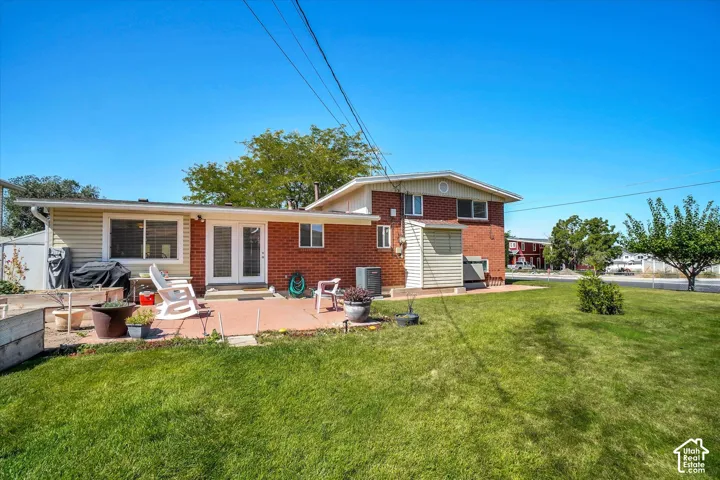 Expansive green lawn, brick and siding exterior, concrete patio, double glass doors, and a storage shed