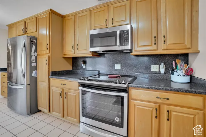 Kitchen featuring wood cabinetry, dark countertops, a stainless steel refrigerator, and a stainless steel oven with a microwave