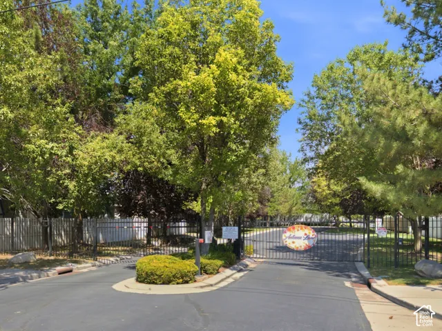 Gated entrance featuring wrought iron fencing, mature trees, and a street lamp