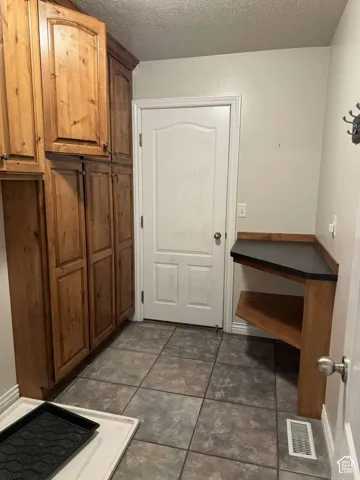 Floor-to-ceiling wood cabinetry, tile flooring, built-in wood shelving with a dark countertop, and a solid core door