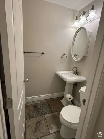 Pedestal sink with a polished chrome faucet, oval mirror, wall-mounted light fixture, and stone tile flooring