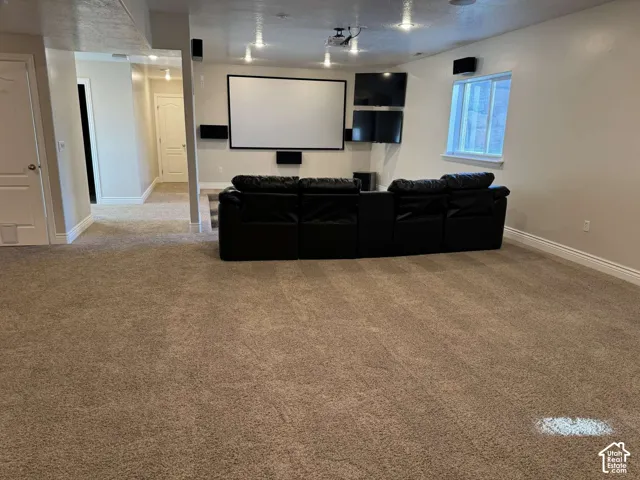 Carpeted recreation room featuring a built-in projector screen, multiple wall-mounted displays, recessed lighting, and a window