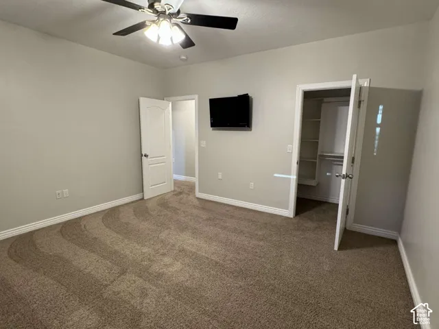Neutral-toned carpeting, ceiling fan with integrated lighting, built-in closet shelving, and a wall-mounted display bracket