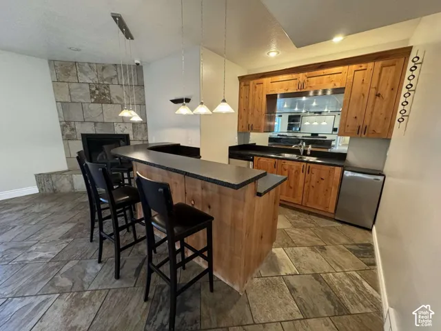 Wet bar featuring natural wood cabinetry, dark countertops, a built-in sink, and stainless steel compact appliances