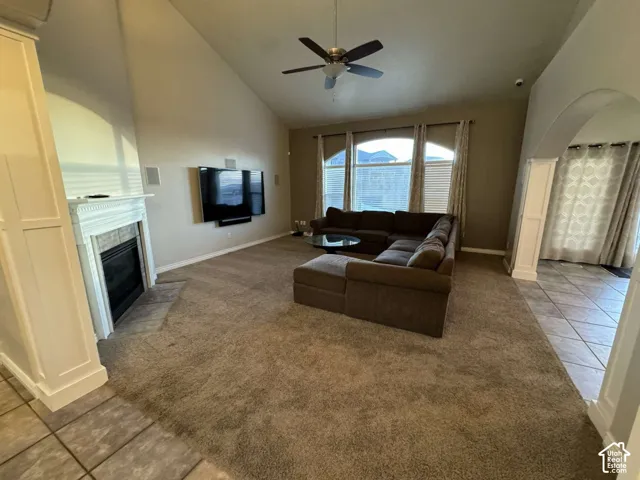 Vaulted ceiling, ceiling fan, fireplace with mantel, archway, and tiled flooring