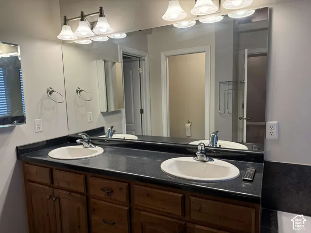 Dual vanity with integrated sinks, dark countertop, wood-finish cabinetry, and overhead lighting fixture