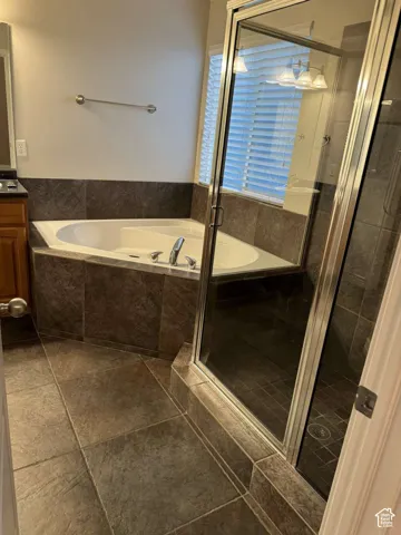 Built-in corner tub with tiled surround, adjacent glass-enclosed shower, and tiled flooring