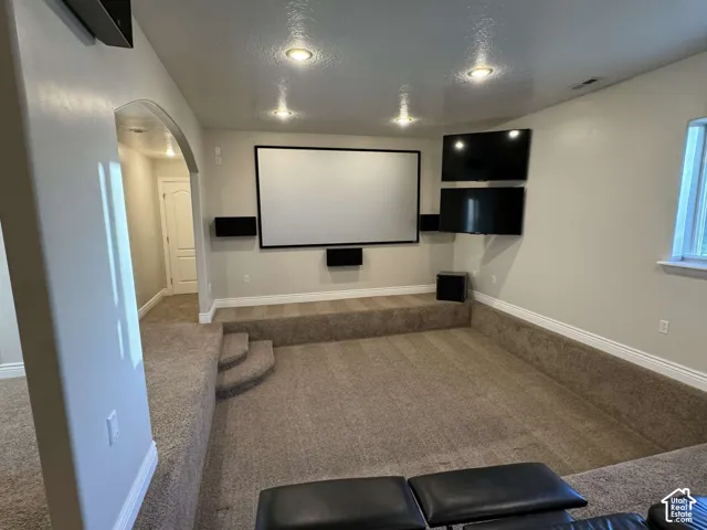 Dedicated media room featuring a large projection screen, dual wall-mounted displays, recessed lighting, and tiered carpeting