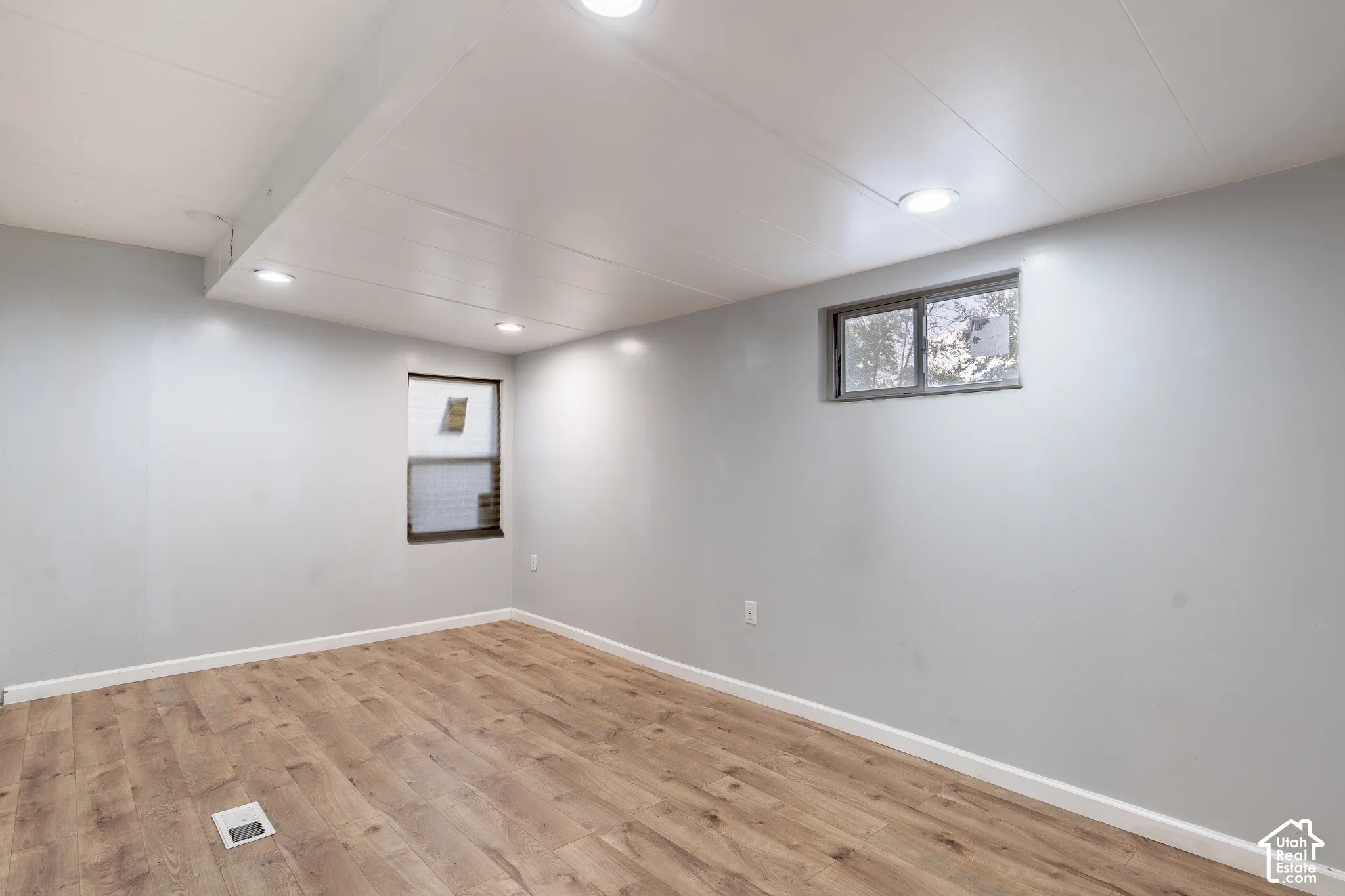 Recessed lighting, light wood-finish flooring, two windows, and light gray wall paint