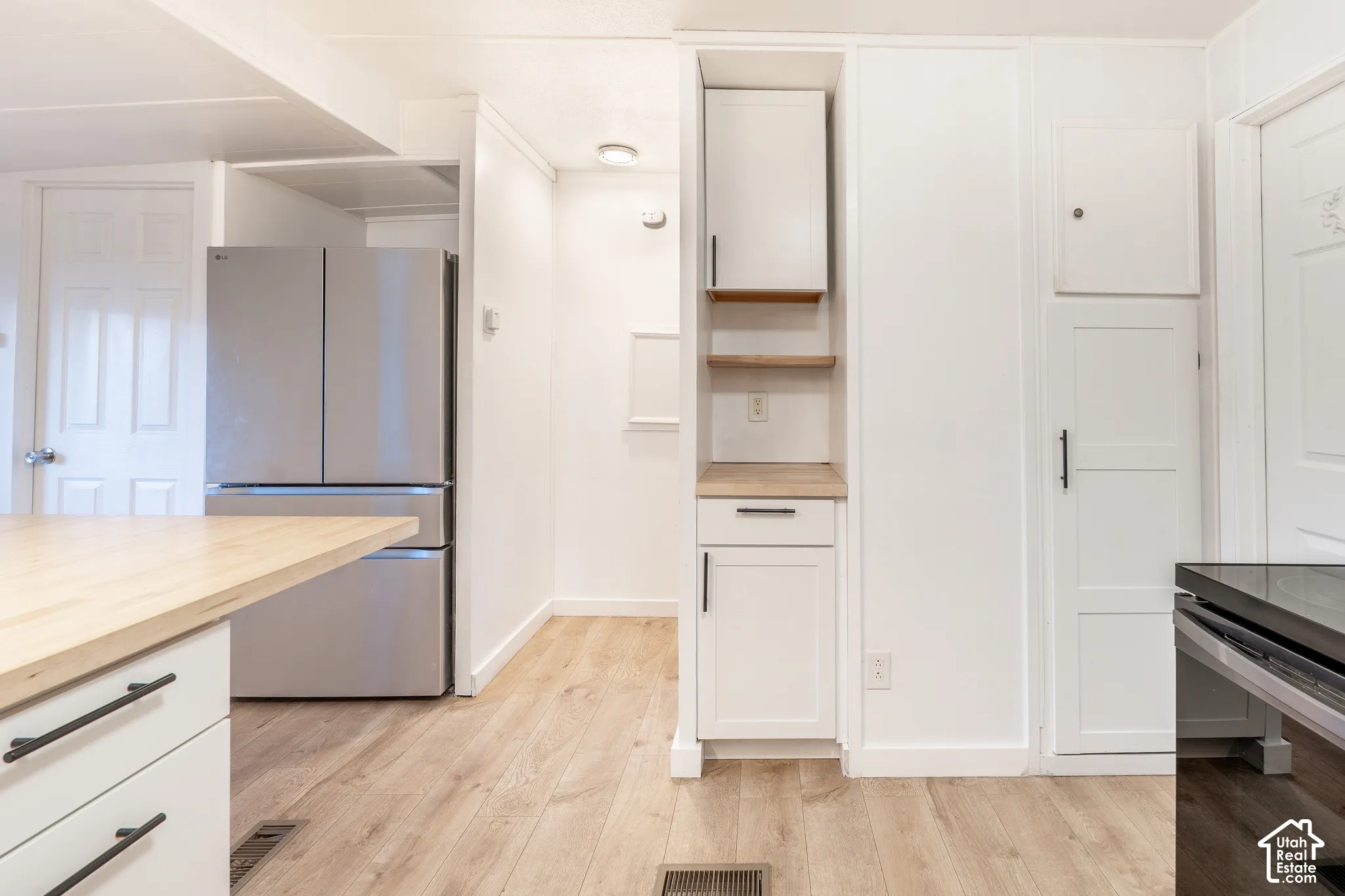 Wood-finish flooring, white cabinetry with black hardware, stainless steel refrigerator, light wood-finish countertop, and built-in shelving