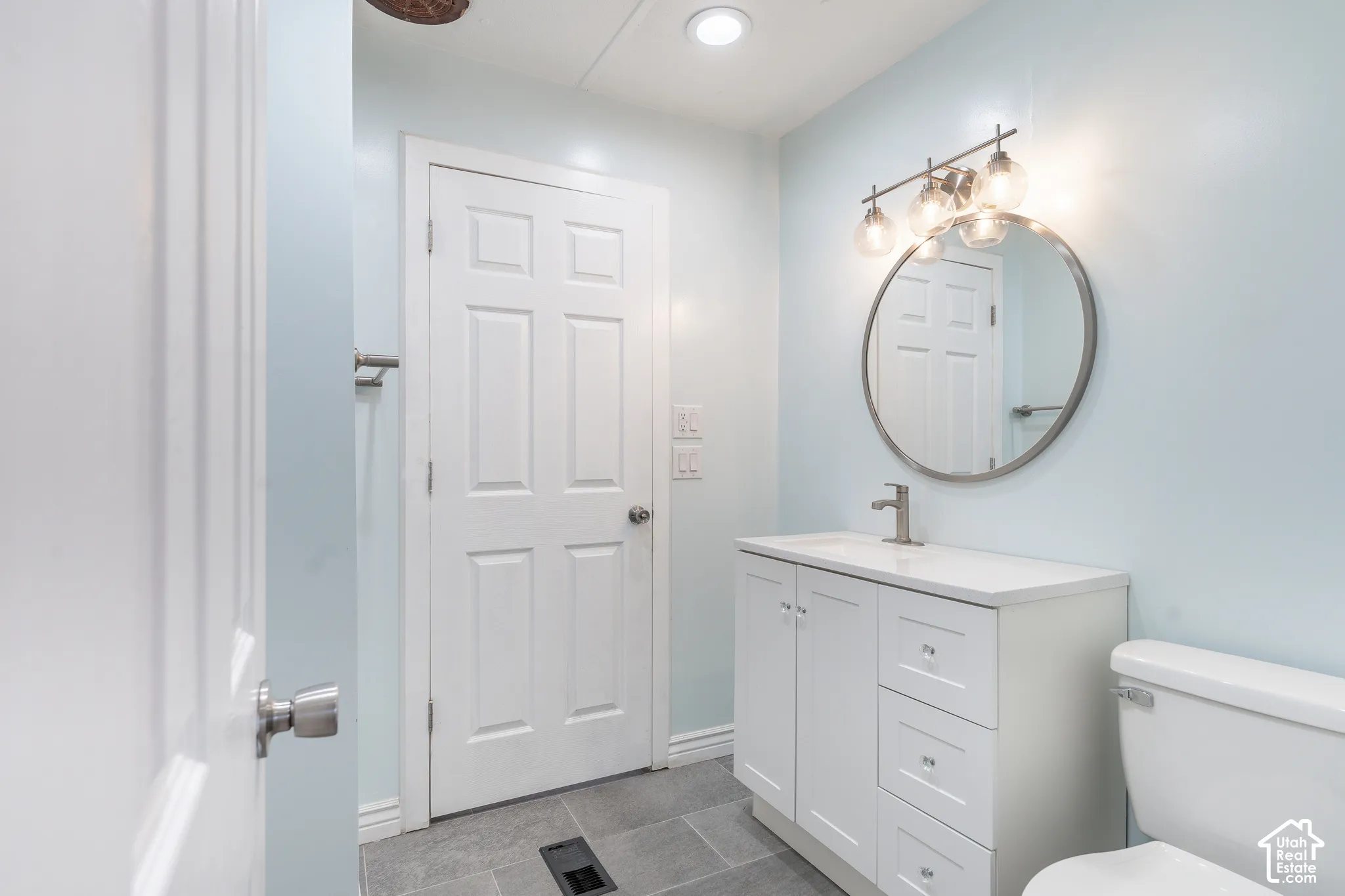 White vanity with an integrated sink, round framed mirror, and a three-light fixture