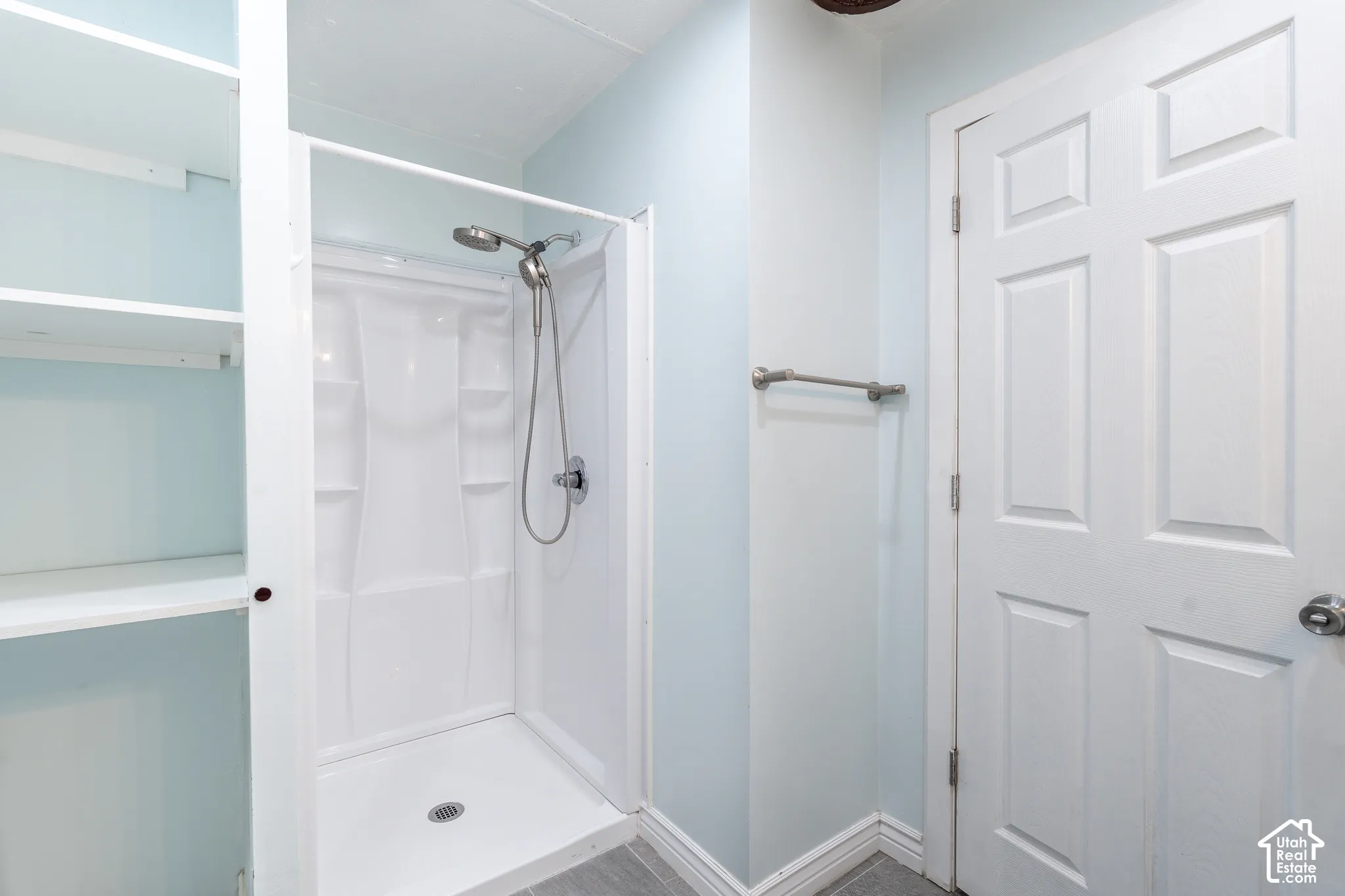 Built-in shelving, white shower enclosure, handheld showerhead, light blue walls, and a paneled door