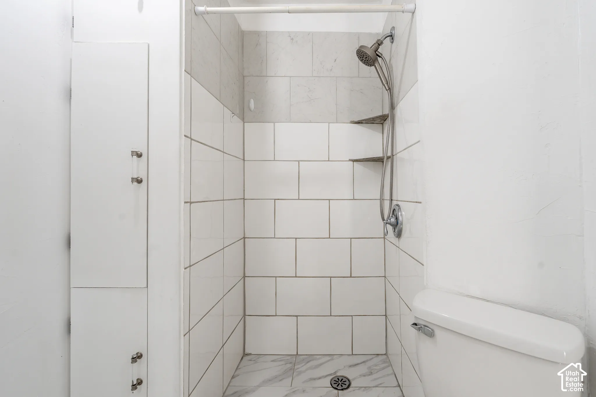 Shower featuring white subway tile, marble-patterned floor, and built-in shelving