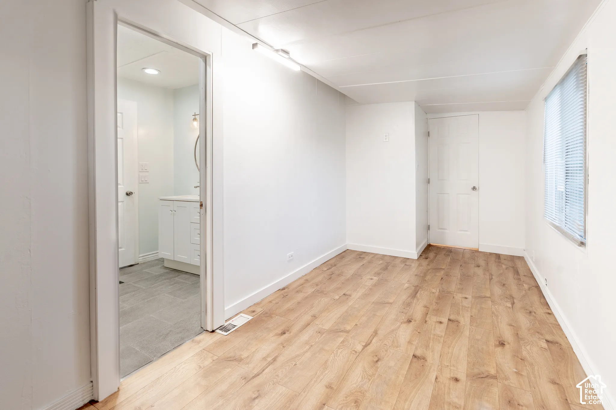 Wood-finish flooring with white baseboards, track lighting, and a window with blinds