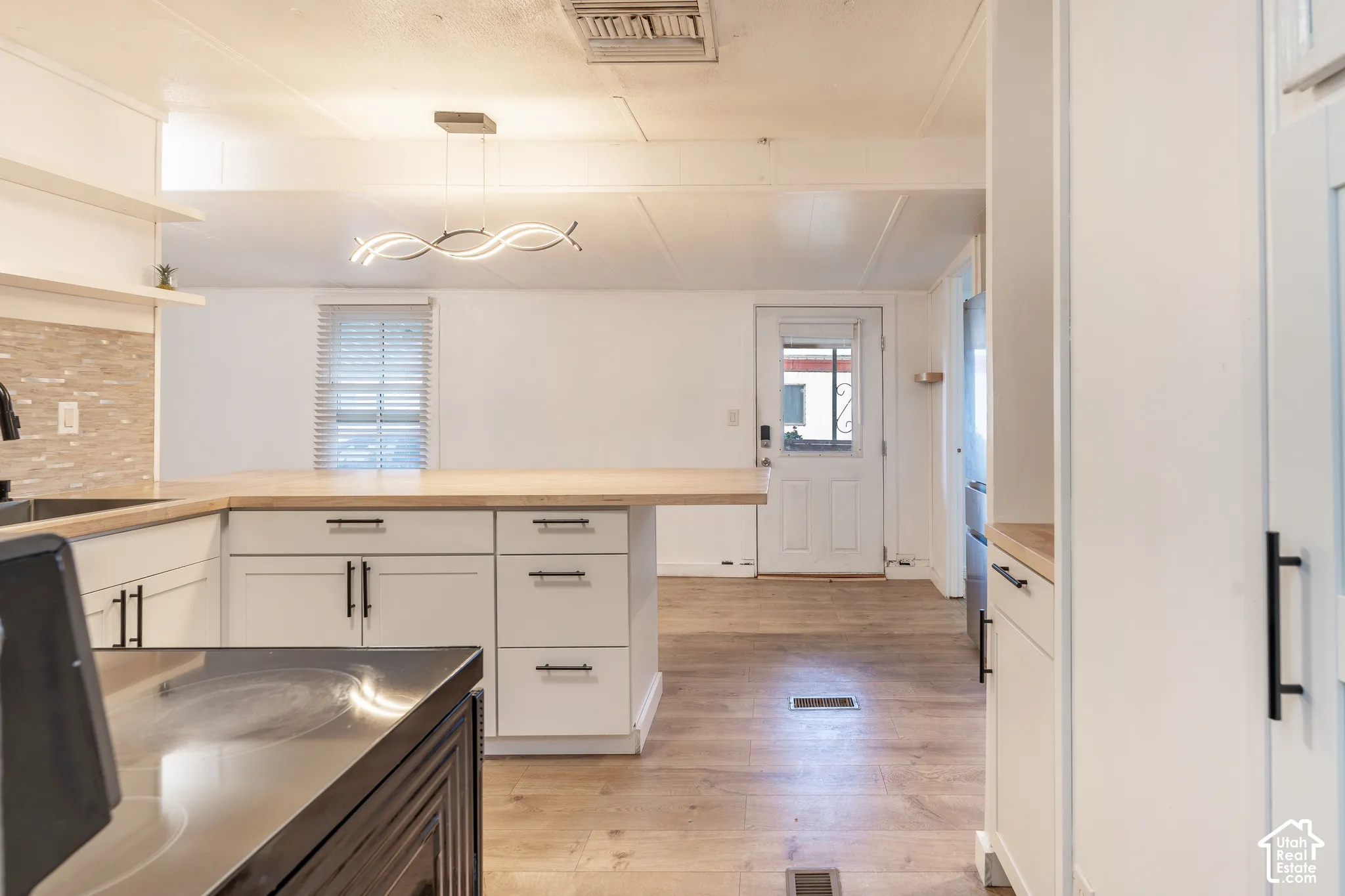 White cabinetry featuring black hardware, wood-finish countertops, wood-finish flooring, and a decorative light fixture
