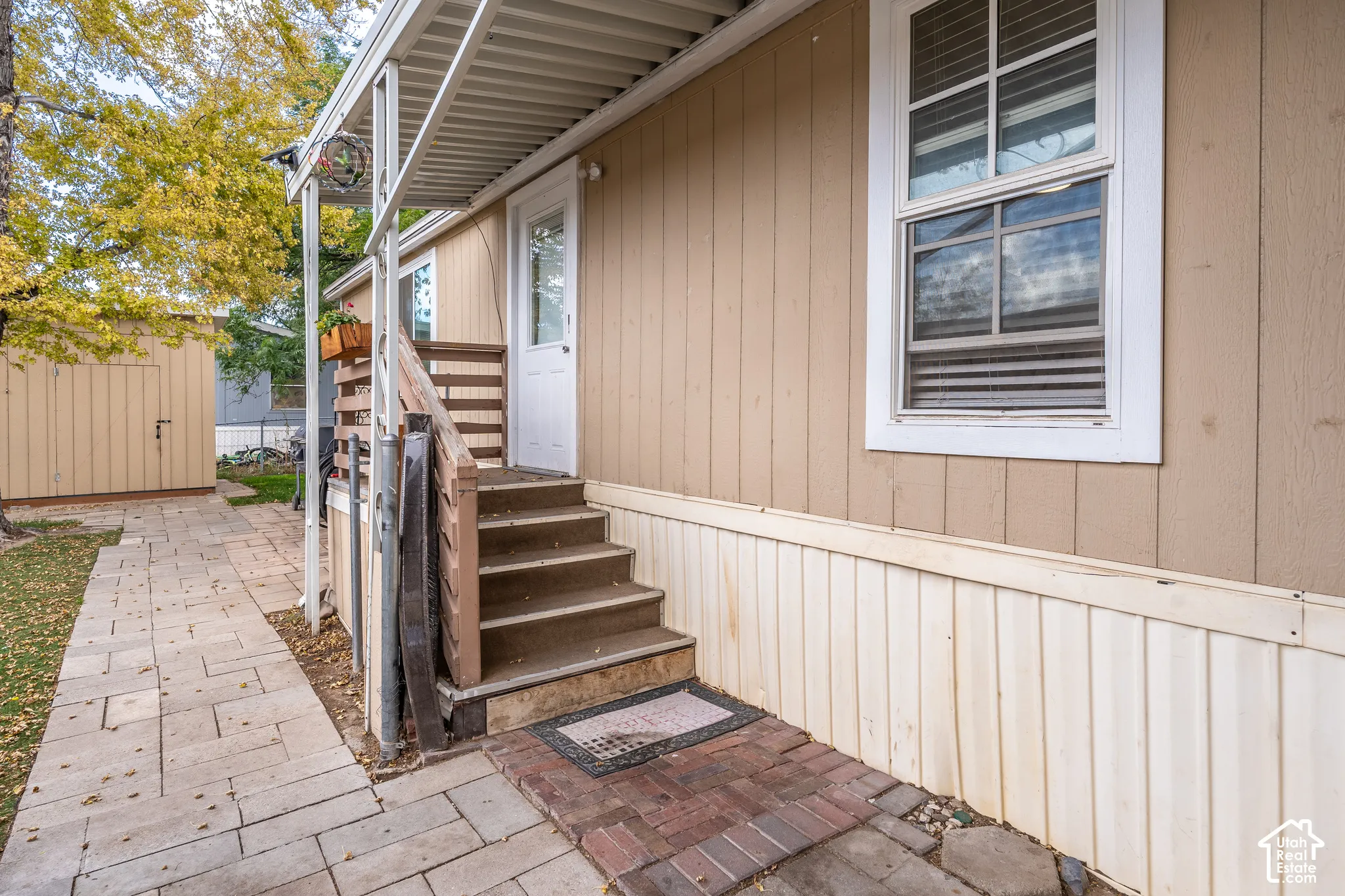 Covered entrance with wood stairs, featuring a paved walkway and a detached storage shed