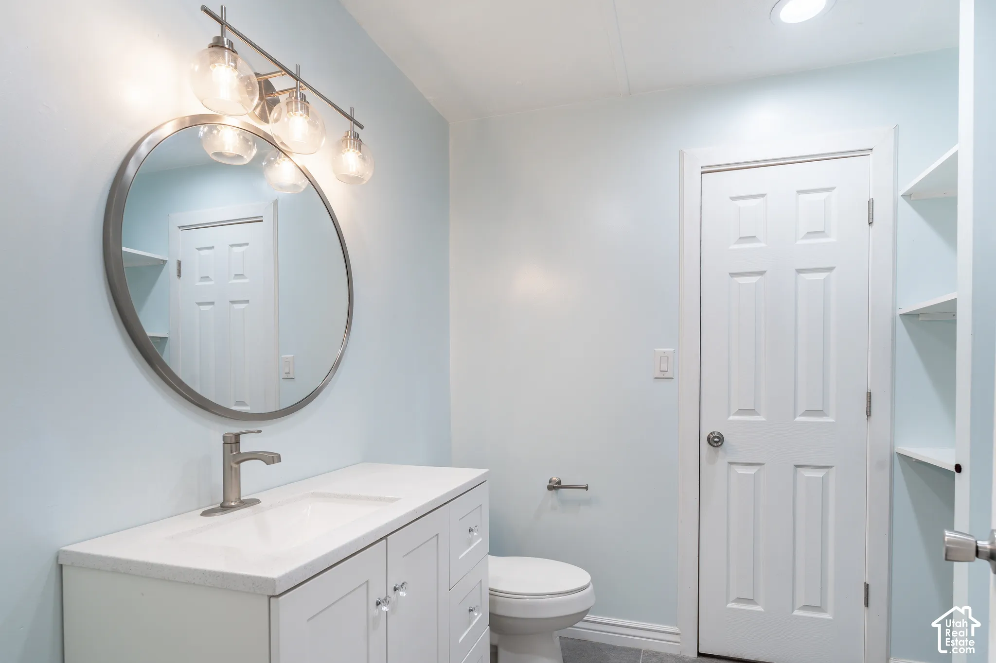 White vanity with a solid surface countertop, brushed nickel faucet, and a circular framed mirror