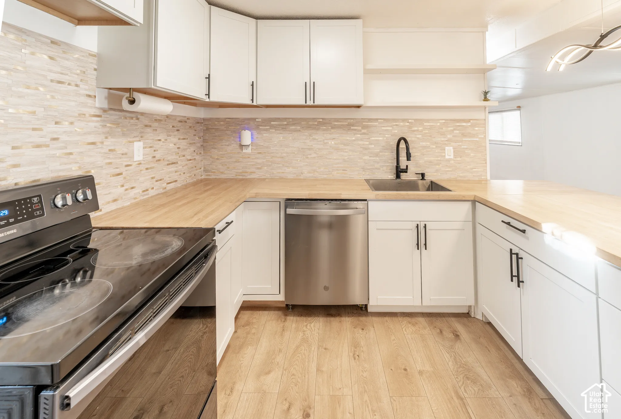 White shaker cabinetry, wood-finish countertops, stainless steel dishwasher, black electric range, and wood-finish flooring