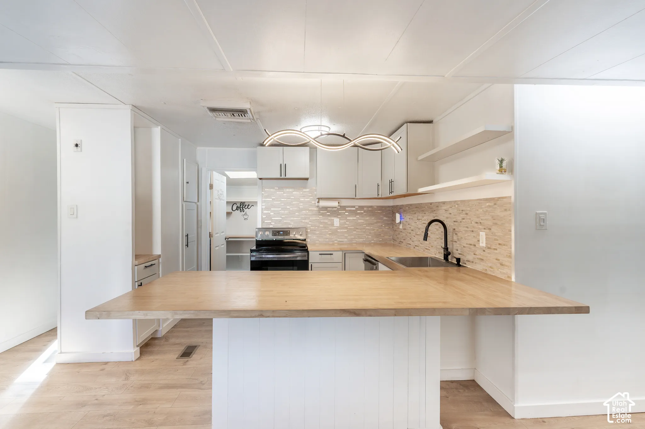Kitchen with light wood-finish flooring, a butcher block style island with seating, white cabinetry, a tiled backsplash, and an undermount sink with a black faucet