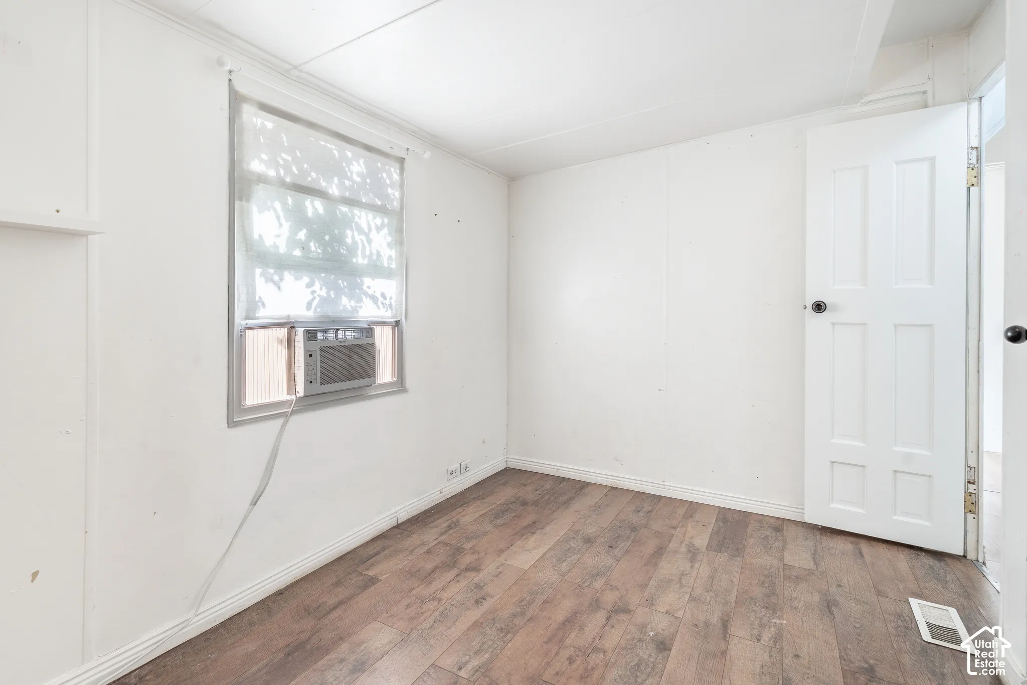 Wood-finish flooring with white baseboards and a window-mounted air conditioning unit