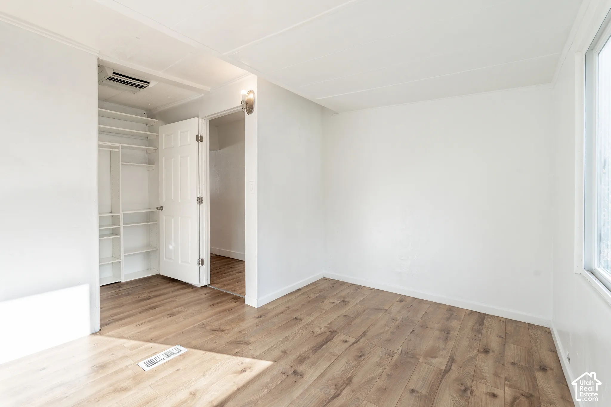 Wood-finish flooring, white walls, built-in closet shelving, and a wall-mounted light fixture