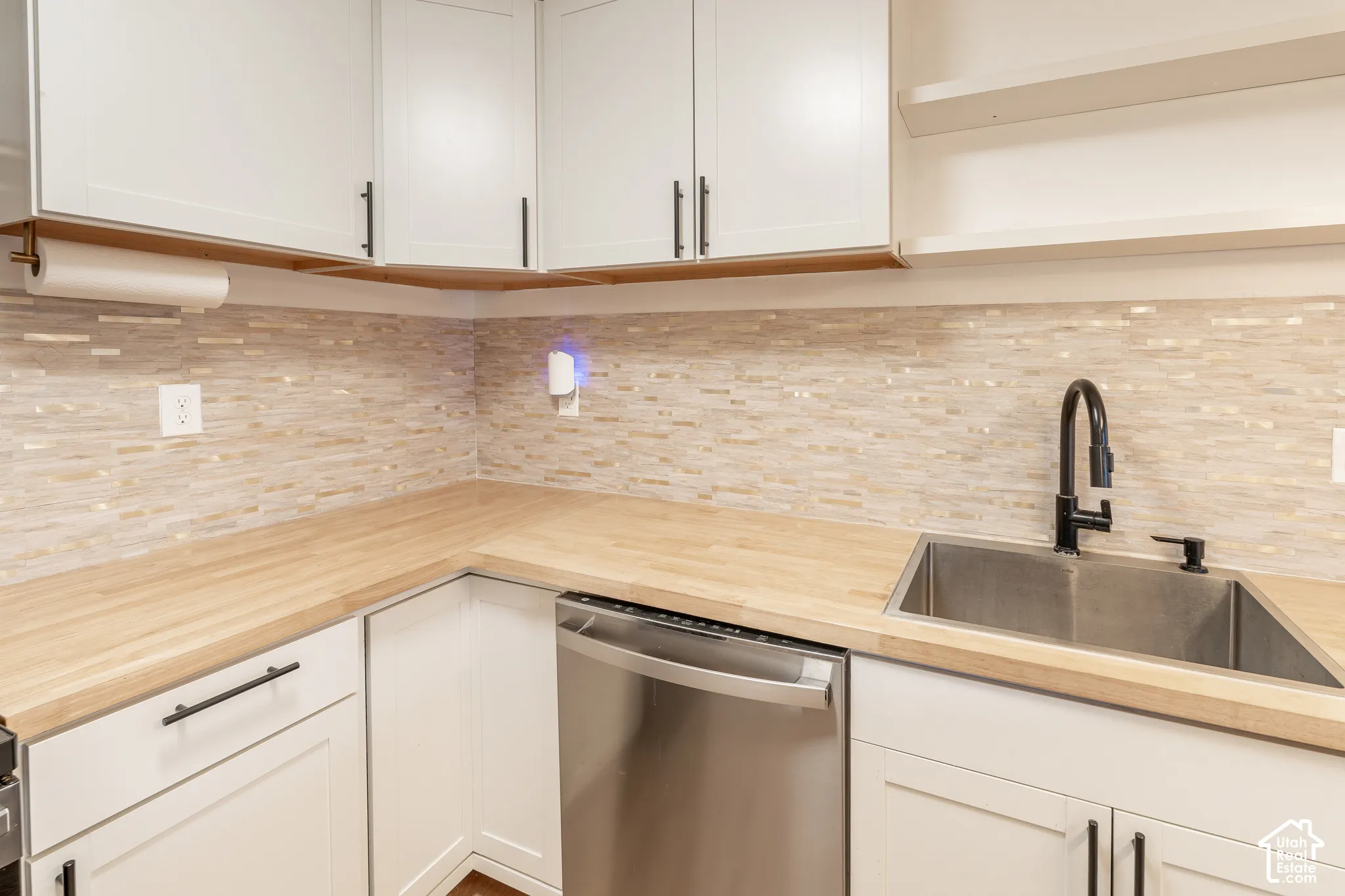 White cabinetry with matte black hardware, wood-finish countertops, tile backsplash, and stainless steel undermount sink