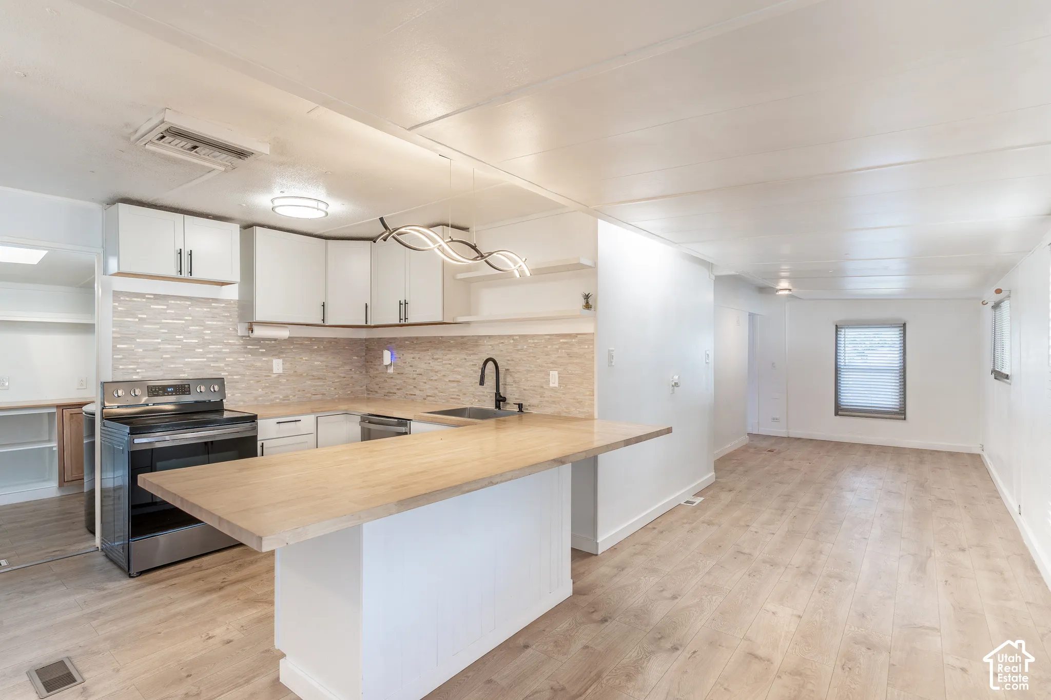 Kitchen featuring stainless steel appliances, light wood-finish countertops, white cabinetry, and a textured backsplash
