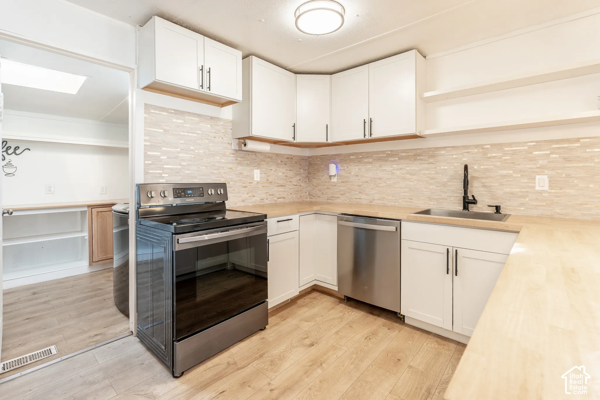 Kitchen with wood-finish flooring, white cabinetry, integrated stainless steel appliances, light-toned backsplash, and a black-finish faucet