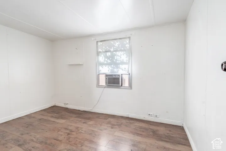 Wood-finish flooring with white panel walls, featuring a window-mounted air conditioning unit and a small wall-mounted shelf