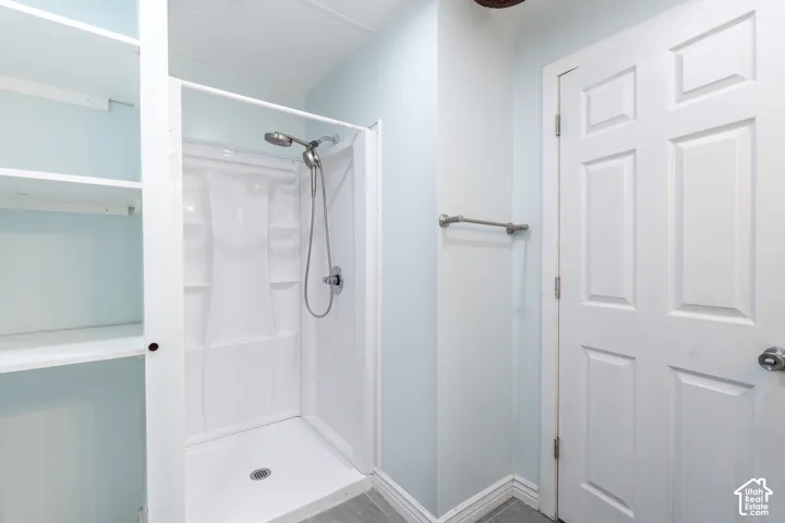 Built-in shelving, white shower enclosure, handheld showerhead, light blue walls, and a paneled door