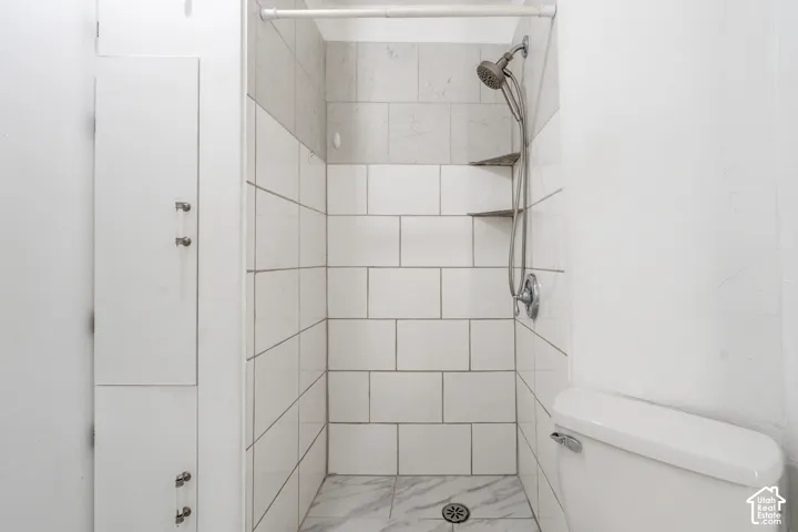 Shower featuring white subway tile, marble-patterned floor, and built-in shelving