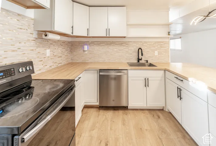 White shaker cabinetry, wood-finish countertops, stainless steel dishwasher, black electric range, and wood-finish flooring