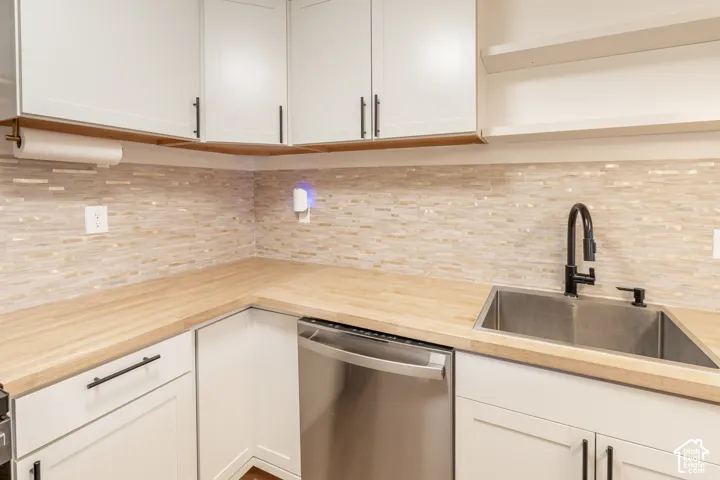 White cabinetry with matte black hardware, wood-finish countertops, tile backsplash, and stainless steel undermount sink