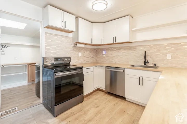 Kitchen with wood-finish flooring, white cabinetry, integrated stainless steel appliances, light-toned backsplash, and a black-finish faucet
