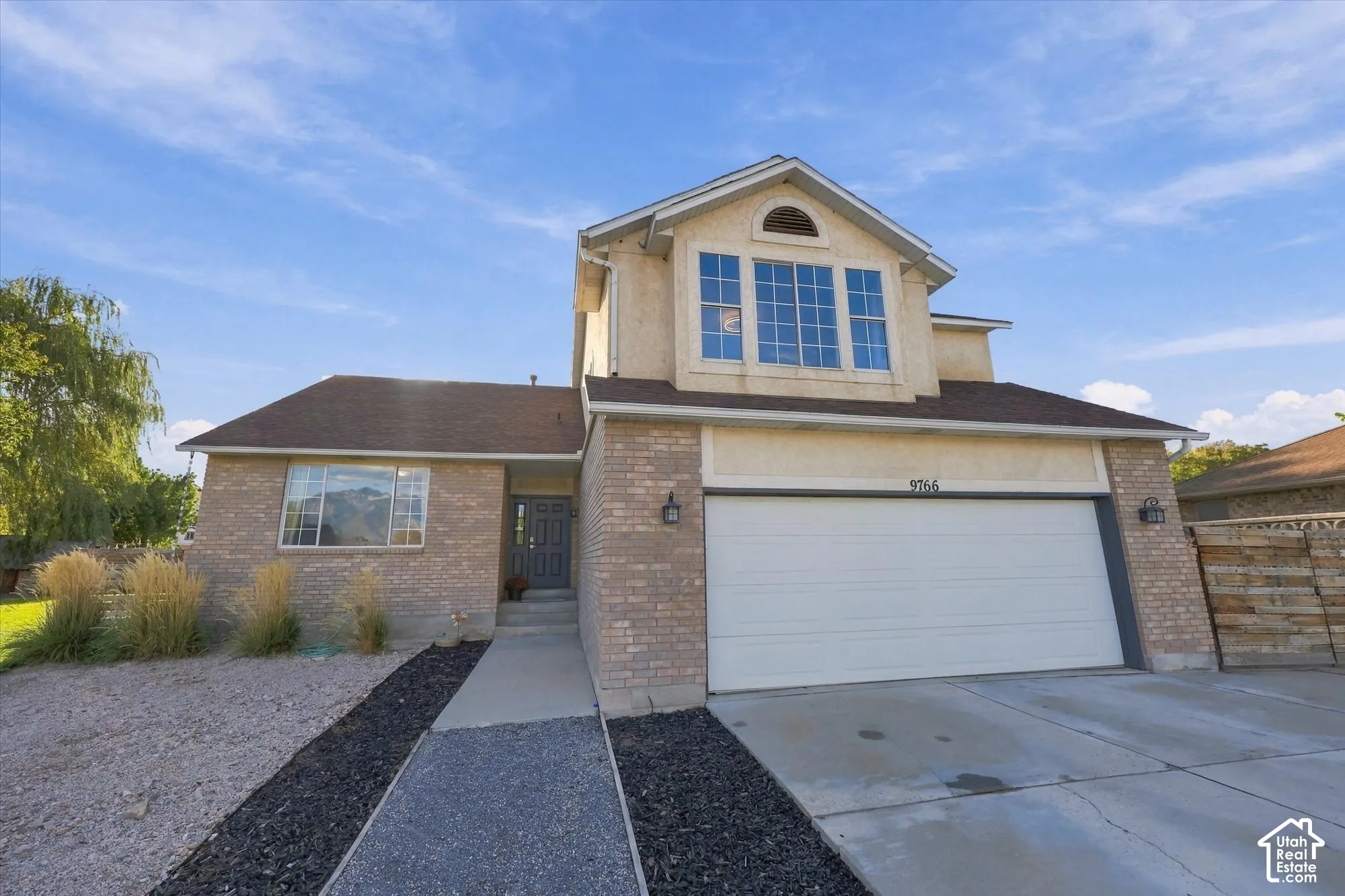 Brick and stucco exterior, prominent bay window, attached two-car garage, concrete driveway, and a paved walkway