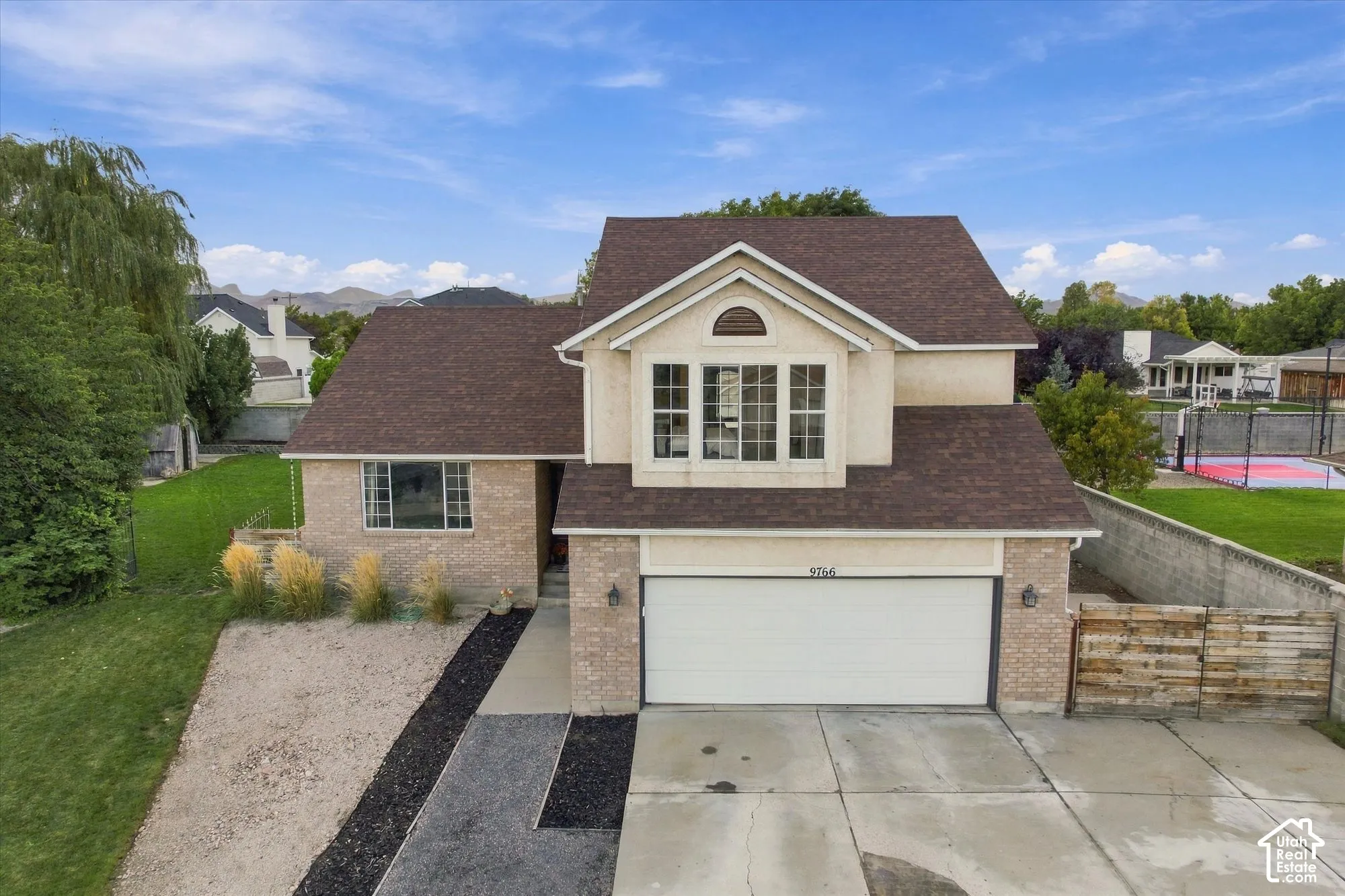 Two-story stucco and brick-clad residence with an attached garage, a paved driveway, and a concrete walkway