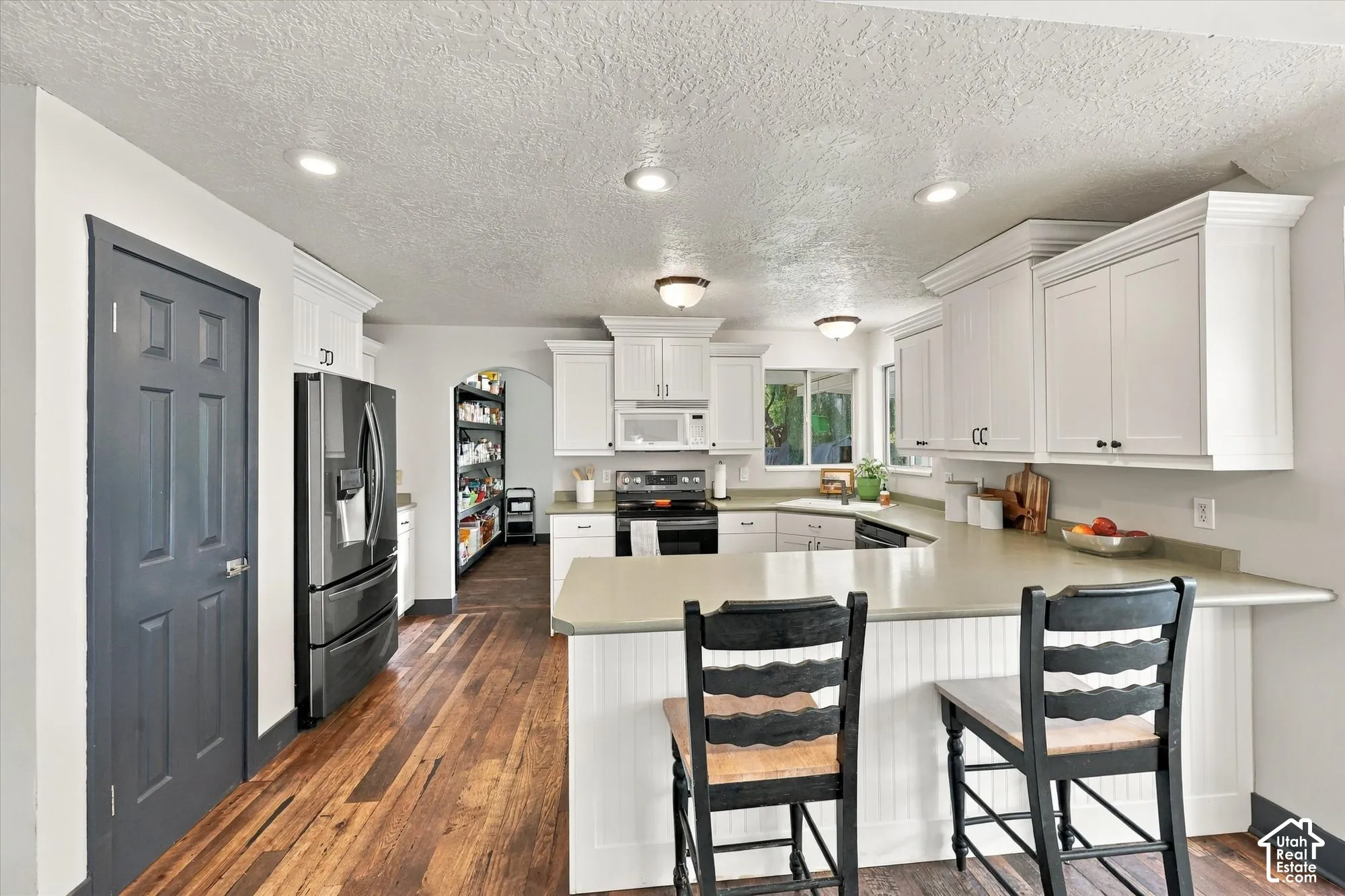 Well-appointed kitchen featuring white cabinetry, light-toned countertops, hardwood flooring, and recessed lighting