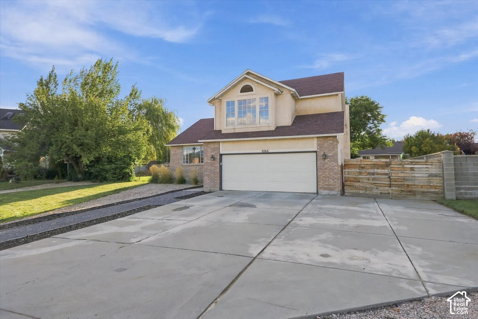Two-story stucco and brick exterior, attached two-car garage, concrete driveway, and a partially fenced yard