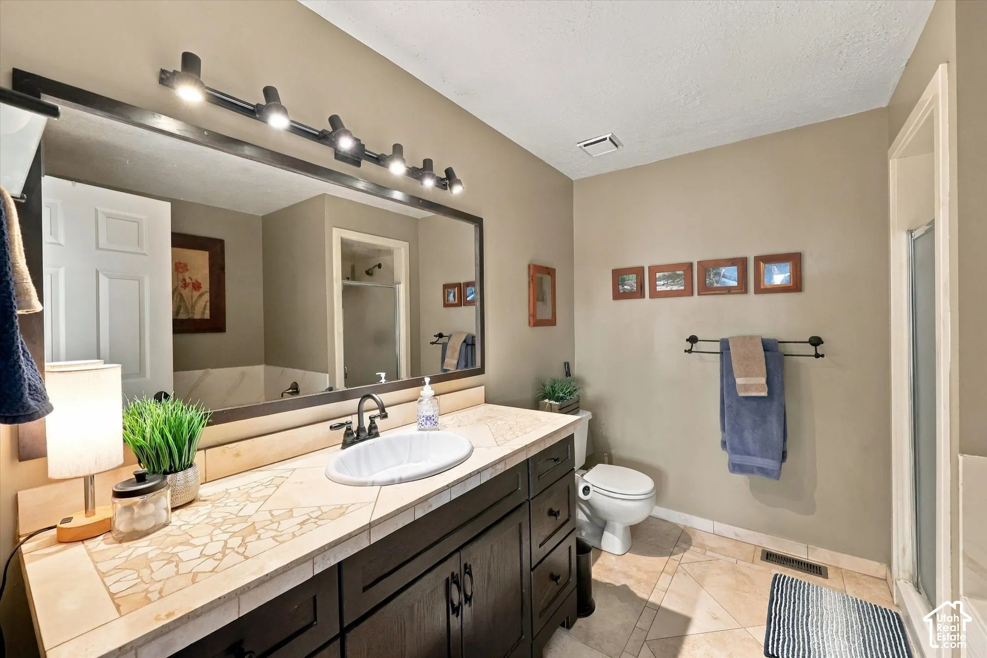 Wood-finish vanity with an integrated basin, tile countertop, and track lighting