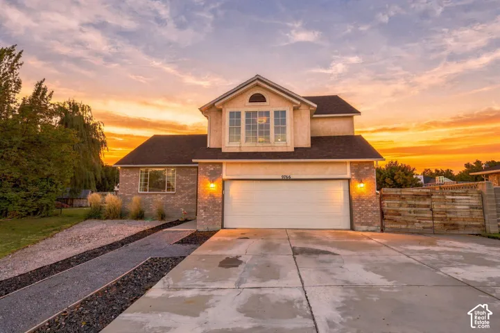 Two-story stucco and brick-clad exterior, big windows, attached garage, and a concrete driveway with gravel accents