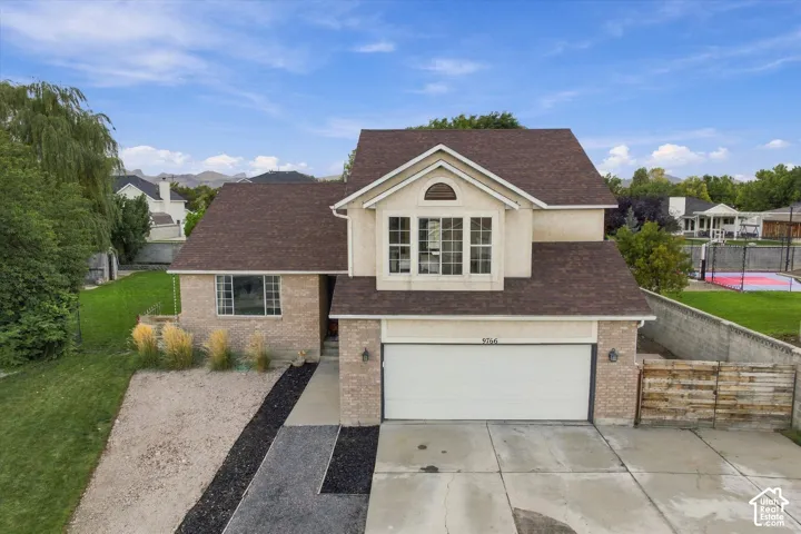 Two-story stucco and brick-clad residence with an attached garage, a paved driveway, and a concrete walkway