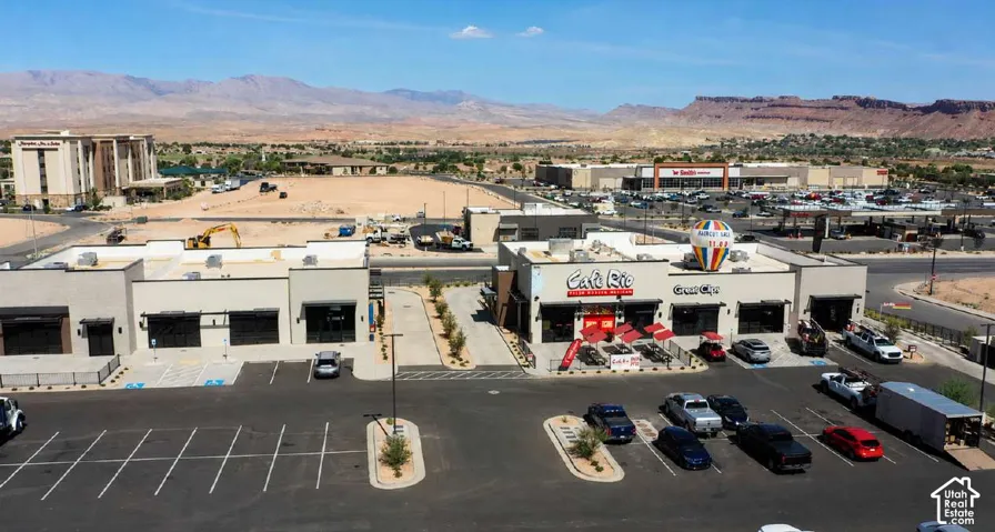 Modern commercial building with multiple storefronts, ample paved parking, and visible mountain backdrop