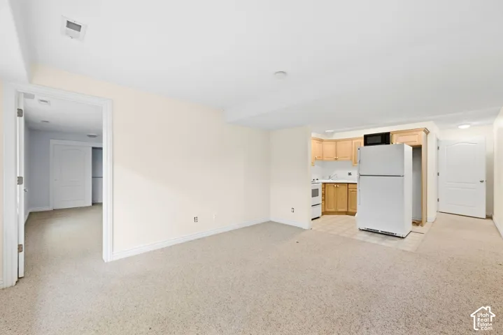 Light-toned carpeting throughout the main area, compact kitchen with wood-finish cabinetry, white appliances, and tiled flooring